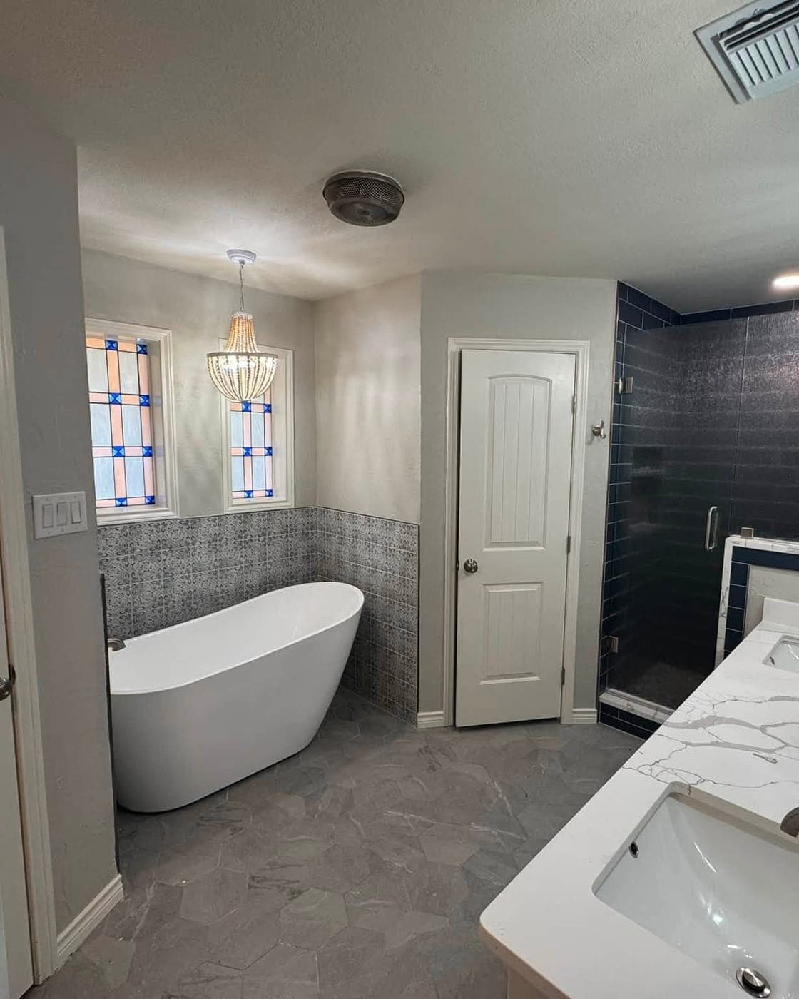 Master bathroom after remodel — freestanding tub, navy tile shower, stained glass